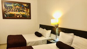 Una habitación de hotel con dos camas, una mesita de noche, una lámpara y un cuadro en la pared.