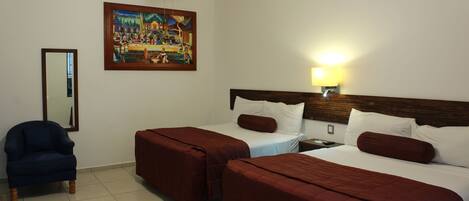 Habitación de hotel con dos camas, una silla, un cuadro en la pared y una mesita de noche con una lámpara.