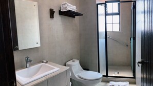Un baño moderno con lavamanos, inodoro y mampara de vidrio.