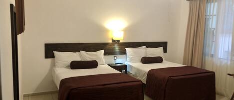 A hotel room with two beds, a ceiling fan, a nightstand, and a window with curtains.