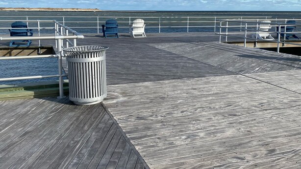 Een houten steiger met een metalen hek, een afvalbak en verschillende Adirondack-stoelen.