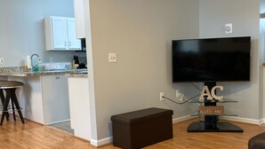 Een moderne woonkamer met een flatscreen televisie, een bank en een keuken in de achtergrond.