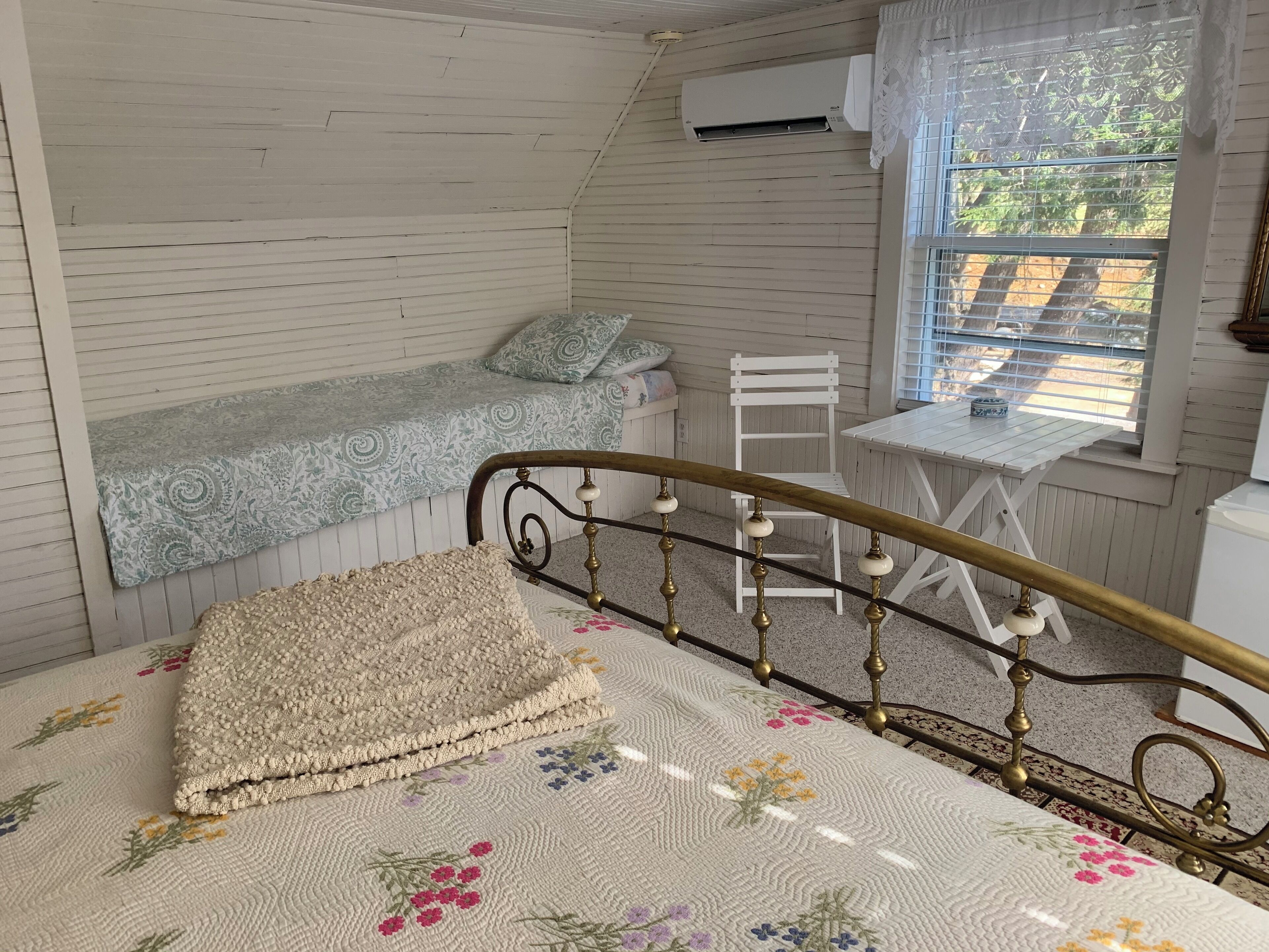 Ein Zimmer mit einem Bett, einem kleinen Tisch, einem Stuhl und einem Fenster mit Jalousien.