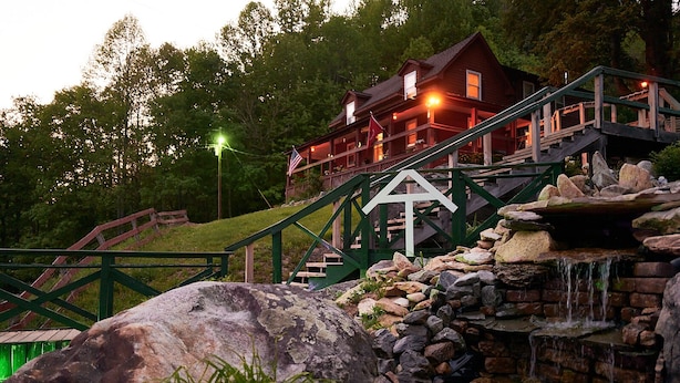 A lodge with a stone waterfall, wooden stairs, and a flag. - Mountain Harbour B&B and Hiker Hostel (Roan Mountain)