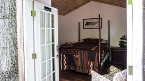 A bedroom with a wooden ceiling, a bed with a patterned bedspread, a nightstand with a ship model, and a door with a 'No Smoking' sign. - Mountain Harbour B&B and Hiker Hostel (Roan Mountain)