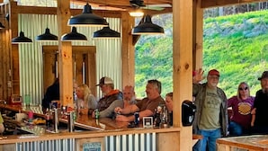 A rustic bar area with wooden beams and hanging pendant lights, overlooking a lush green hillside. - Mountain Harbour B&B and Hiker Hostel (Roan Mountain)