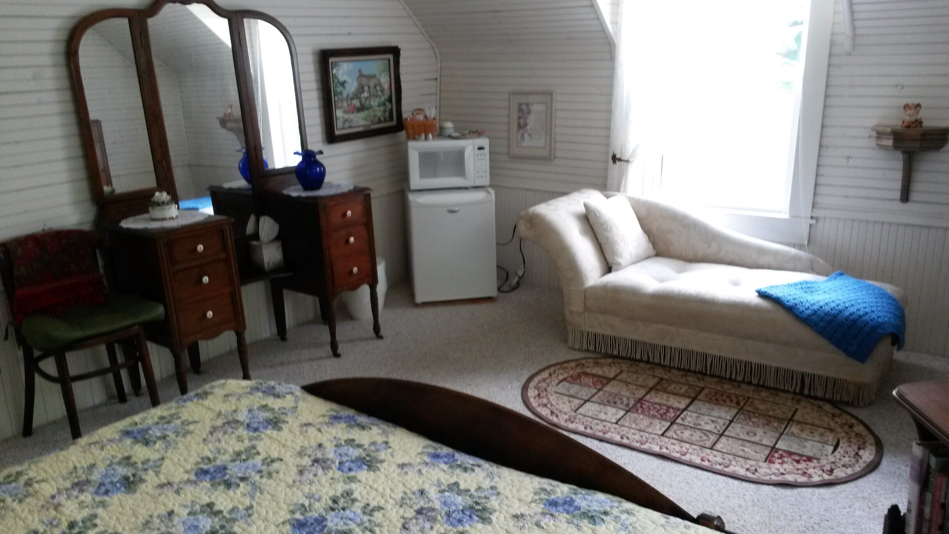 Une pièce comprenant un lit, un bureau, une chaise, une commode, un canapé, un four à micro-ondes et une fenêtre.