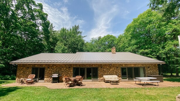 A stone building with a metal roof, outdoor seating, and a grill.