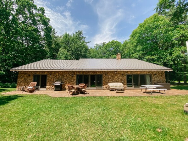 A stone building with a metal roof, outdoor seating, and a grill.
