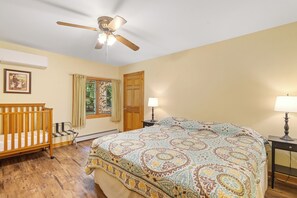 A bedroom with a bed, a crib, a ceiling fan, a window with curtains, and a door. - Secluded Family- and Pet-Friendly Cottage (New Era)
