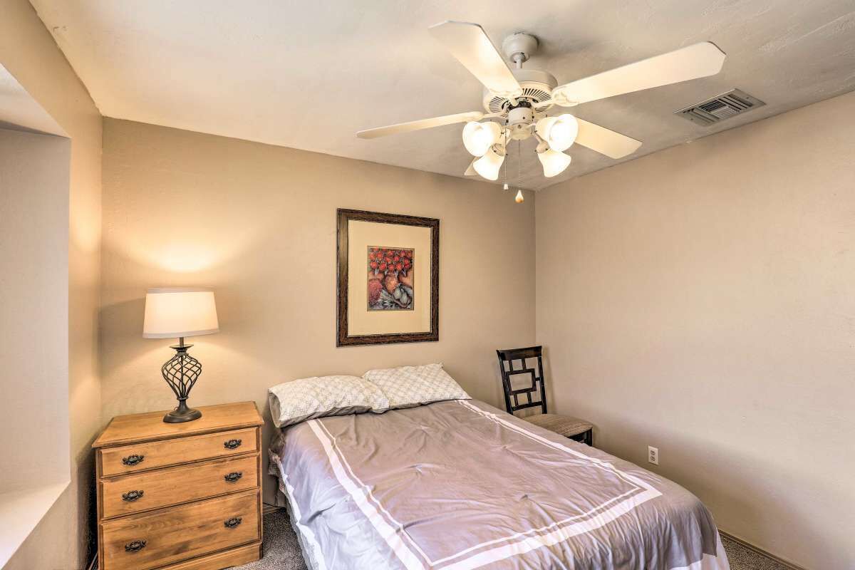 A bedroom with a bed, a nightstand, a lamp, a chair, and a ceiling fan.