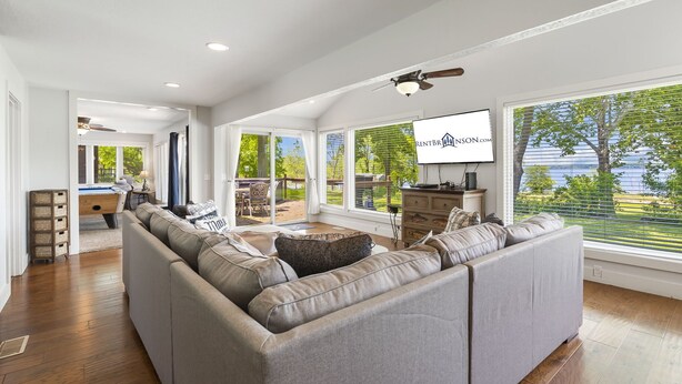 A spacious living room with a large sectional sofa, a ceiling fan, and a TV mounted on the wall.