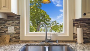 A kitchen with a stainless steel sink, a window with a view of trees, and a backsplash with a mosaic tile pattern.