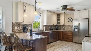 A kitchen with white cabinets, a granite countertop, a stainless steel refrigerator, and a ceiling fan.