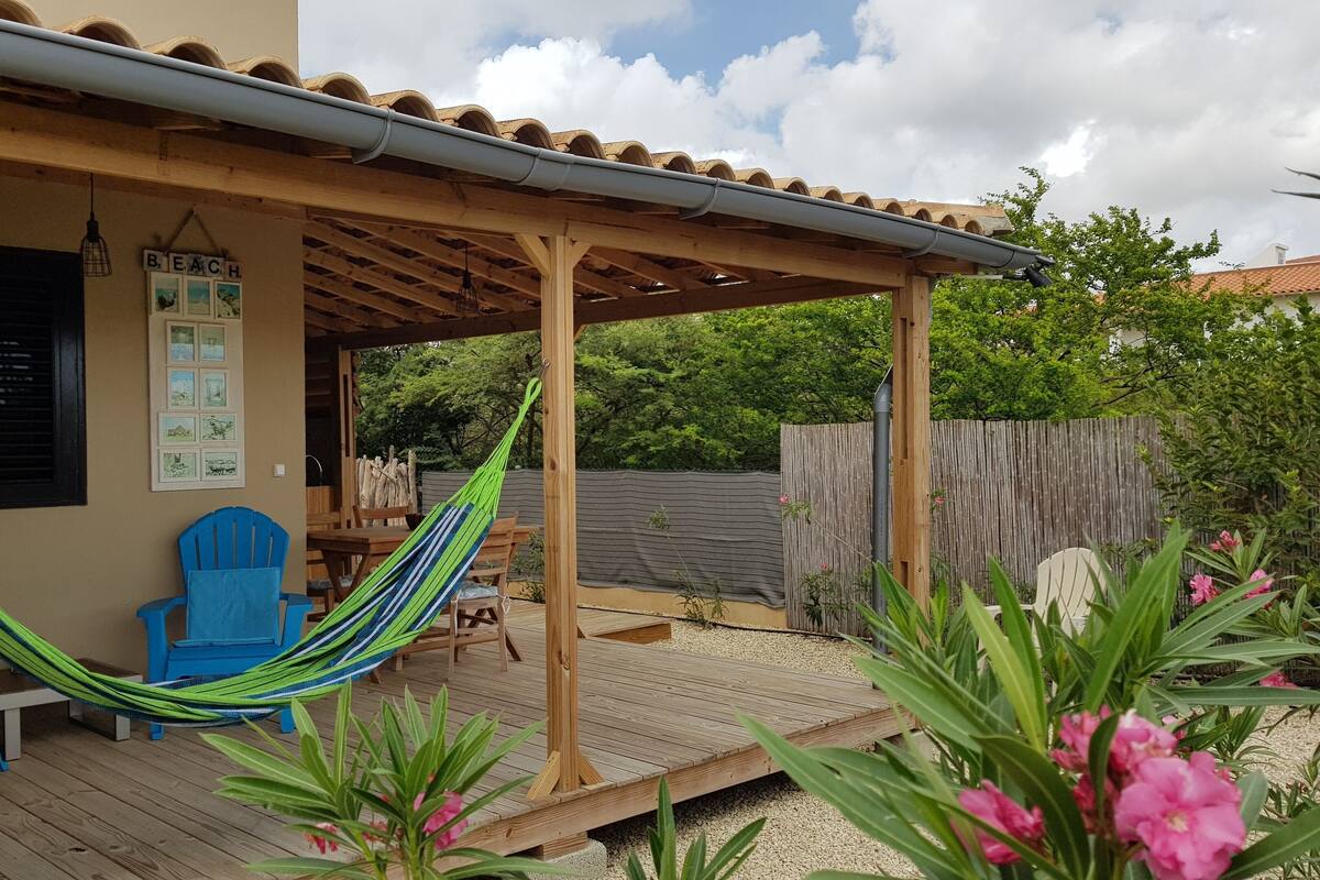 A covered patio with a wooden deck, a hammock, and a blue chair.