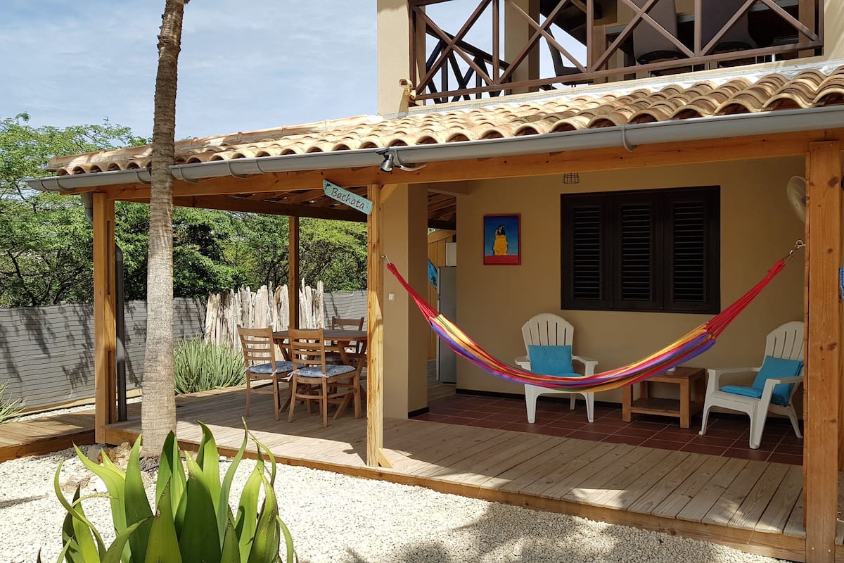 A covered patio area with wooden furniture, a hammock, and a view of the house's exterior.