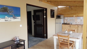Una cocina acogedora con armarios de madera, una mesa de comedor con sillas y vistas al mar a través de un ventanal abierto.