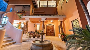 A modern house with a stone fountain, a wooden staircase, and a large wooden door.
