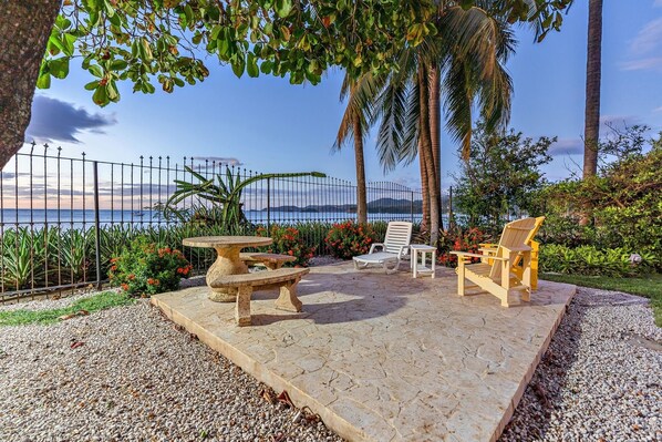 An outdoor seating area with a table and chairs, a view of the sea, and a fence.