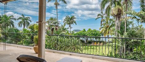 A balcony with a view of palm trees and a grassy area.