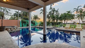 A pool area with clear blue water, surrounded by palm trees and lounge chairs.