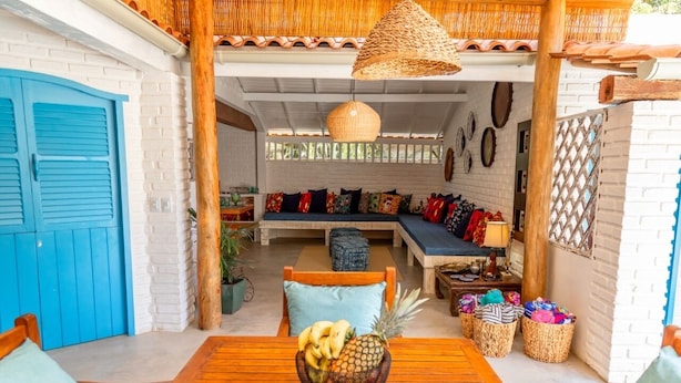 A cozy patio area with a wooden table, a bowl of fruit, and wicker baskets. - Casa BluMarino (Porto Seguro)
