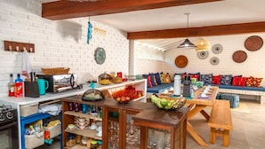 A cozy kitchen and dining area with a white brick wall, wooden beams, and a variety of colorful dishes and utensils. - Casa BluMarino (Porto Seguro)