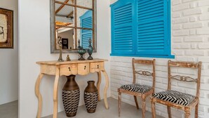A room with a white brick wall, a wooden console table with two vases, a mirror, and two chairs with zebra-patterned cushions. - Casa BluMarino (Porto Seguro)