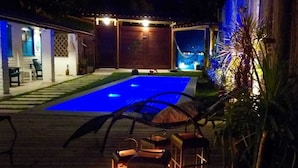 A pool area with a blue-lit water feature, surrounded by a wooden deck and outdoor furniture. - Casa BluMarino (Porto Seguro)