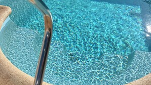 Una piscina interior luminosa con barandilla de metal, suelo de baldosas y vistas al cielo a través de un ventanal.