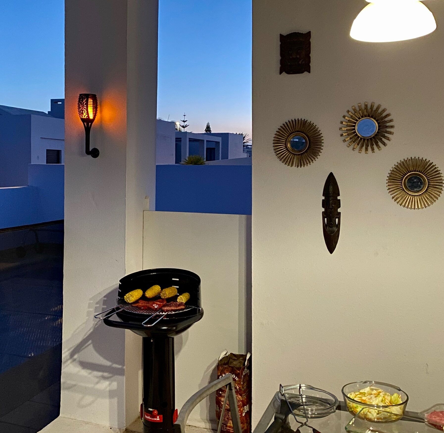 A balcony with a barbecue grill, decorative wall art, and a view of buildings in the background.
