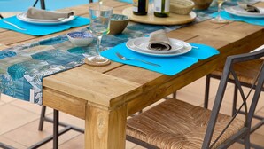 Una mesa de comedor de madera dispuesta con platos, vasos y cubiertos, con una piscina al fondo.