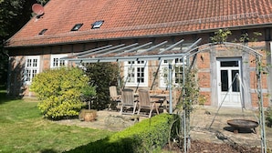 Een huis met een rood pannendak, een bakstenen gevel en een overdekte patio met tuinmeubilair.