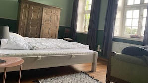 Een slaapkamer met een bed, een houten garderobe, een nachtkastje, een stoel en een raam met gordijnen.