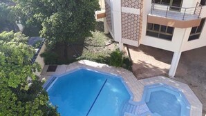 Zona de piscina en la azotea con dos piscinas, rodeada de árboles y un edificio con balcón.