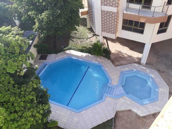 Un espace piscine sur le toit, comprenant deux piscines, entouré d’arbres et bordé d’un immeuble doté d’un balcon.