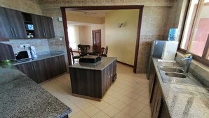Una cocina con encimeras de granito, una isla central y un área de comedor visible a través de un vano abierto.