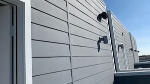 Un bâtiment dont le revêtement extérieur est de couleur grise, avec une porte blanche et plusieurs luminaires d’extérieur.