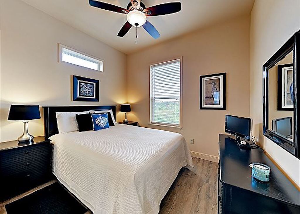 Une chambre à coucher avec un lit, des lampes de chevet, un ventilateur de plafond, une fenêtre et des tableaux encadrés accrochés au mur.