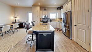A spacious kitchen with a central island, white cabinetry, and a dining area with a table and chairs. - Gorgeous beach views Walk to beach Theater room (Gulf Shores)