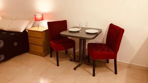 Une petite pièce comprenant un lit, une table de chevet avec une lampe, une table avec deux chaises et deux verres à vin.