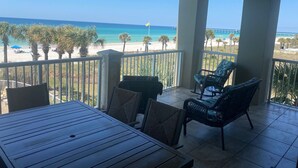 A balcony with a view of the beach, palm trees, and a pier. There are wicker chairs and a wooden table. - September Reduced Rates !! VIP Beach Chair service Included (Panama City Beach)