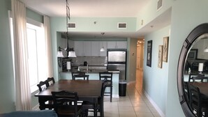 A modern kitchen with a dining area, featuring a central island, pendant lighting, and a large mirror on the wall. - September Reduced Rates !! VIP Beach Chair service Included (Panama City Beach)