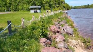 A lakeside view with a grassy area, a small building, and a wooden fence along the water's edge. - Waterfront Private Campground-Two extra RV hookups available - 50.00 per night   (Ontonagon)