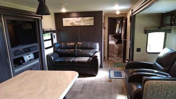 A compact RV interior with a kitchenette, a seating area with a couch and chairs, and a mounted television. - Waterfront Private Campground-Two extra RV hookups available - 50.00 per night   (Ontonagon)