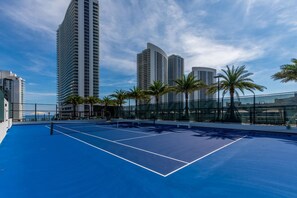 A tennis court with a blue surface, surrounded by tall buildings and palm trees. - HYDE HOUSE NEW (Hollywood)