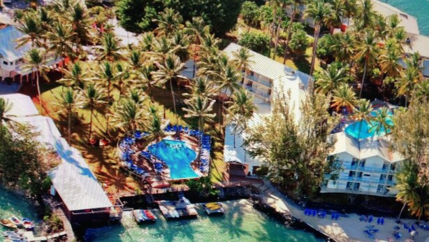 An aerial view of a resort with a central pool surrounded by palm trees and beach umbrellas. - Beautiful, air-conditioned studio in a 3-star hotel: 2 pools + INTERNET, right on the water (Les Trois-Îlets)