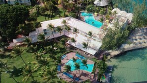 An aerial view of a resort with multiple swimming pools, palm trees, and beach umbrellas. - Beautiful, air-conditioned studio in a 3-star hotel: 2 pools + INTERNET, right on the water (Les Trois-Îlets)