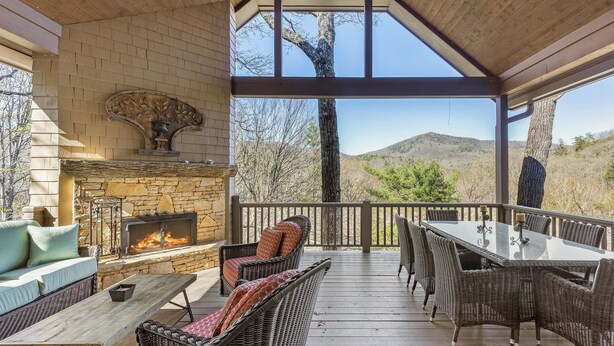 A covered outdoor patio with a stone fireplace, wicker furniture, and a view of the surrounding landscape. - Fawn Creek: Beautifully Appointed, Mtn Views w Covered Porch and Wood Fireplaces (Highlands)