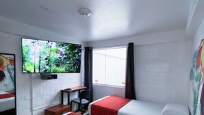 A hotel room with two beds, a desk, a chair, a TV, and a window with curtains. - Magdalen House (Lima)